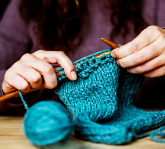 Mains tricotant avec laine teinte bleu turquoise et aiguilles en bois