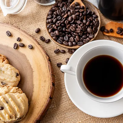 Café noir dans tasse avec scones et grains de café sur table en tissu.